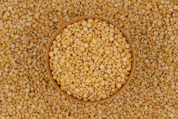 Raw yellow split peas in a wooden plate on a background of pea texture