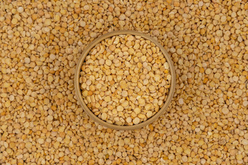 Raw yellow split peas in a wooden plate on a background of pea texture
