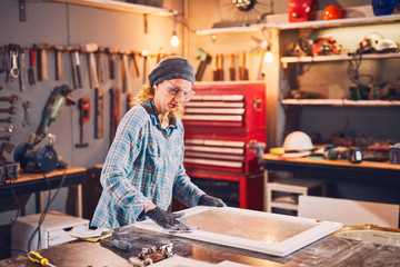 Woman carpenter sanding old window in a retro workshop.