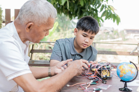 STEM education, Asian boy and retired grandfather learning programming process of new robot technology. Happy family members relationship, Studying anywhere anytime to learn together at home outdoor