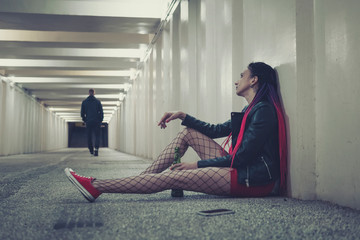 Girl sitting on the floor in the tunnel with a bottle of whiskey and looks at the outgoing of a guy...