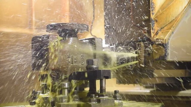 The process of drilling and grinding holes in the body of the valve on the CNC machine. Yellow-green coolant splashes into place