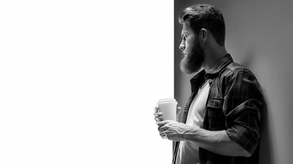 Side view of young bearded man with paper coffee cup in his hand
