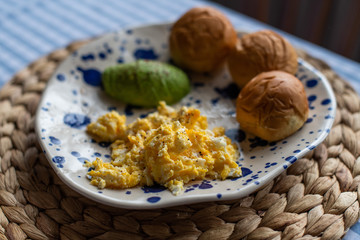 breakfast plate of scrambled eggs, sliced avocado and small sandwich bread.