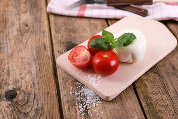 mozzarella cheese with fresh tomatoes and basil on a rustic wooden table 