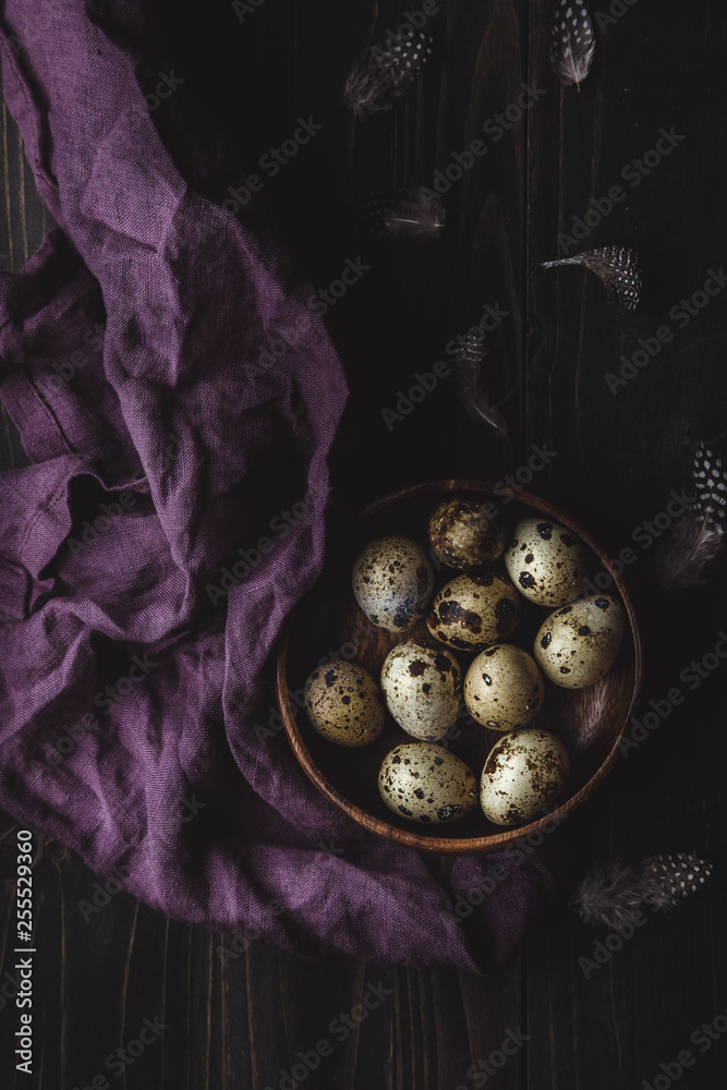 Wall mural Quail eggs in wooden bowl with feathers on dark wooden background.