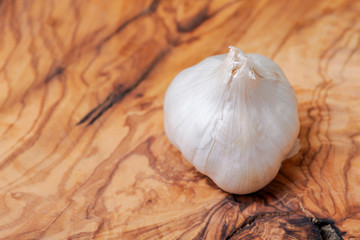 Organic Raw Whole Garlic bulb placed on natural olive wood. Allium sativum.