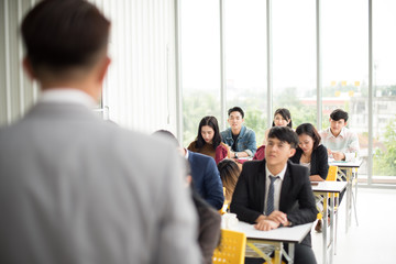 Asian male speaker is speaking at seminars and workshops to the people in the meeting. Participants are raising their hands to ask questions.