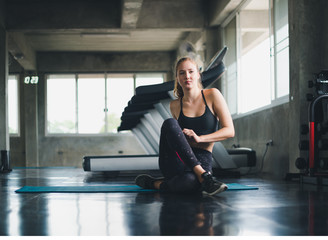 Beautiful athlete put on a sports suit. Stretching a muscle on a yoga mat. Before playing sports in the gym. She is relaxing