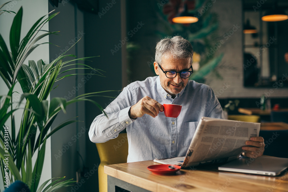 Wall mural coffee break. man drinking coffee and reading newspaper in cafe bar