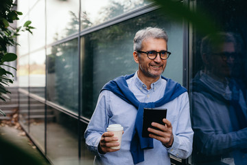 senior businessman using tablet beside glass building outdoor