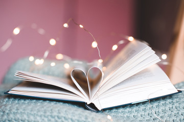 Open book with folded sheets in heart shape closeup over lights. Love stories.
