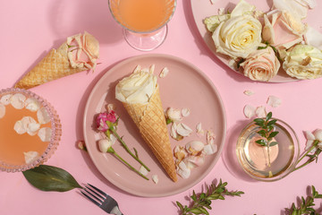 Light pink set of dishes on the table. Delicate rosebuds of pastel colors and petals on a plate and waffle cones. Top view.