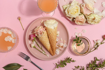 Light pink set of dishes on the table. Delicate rosebuds of pastel colors and petals on a plate and waffle cones. Top view.