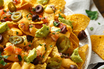 Mexican nachos tortilla chips with olives, jalapeno, guacamole, tomatoes salsa and cheese dip. close up