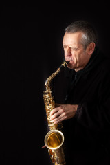 Fototapeta premium A Musician playing jazz music on his saxophone, on black background