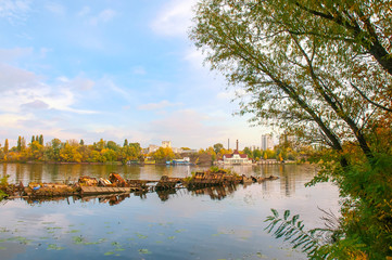 Wrecked boat on the Dnieper river in Kiev, Ukraine, in autumn. In the background, ypou can see an uninhabited floating house. Light clouds float in a pale blue sky