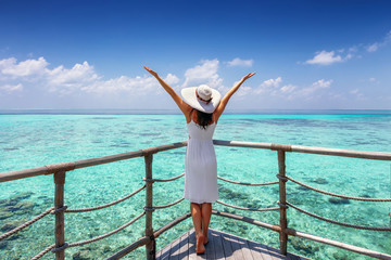 Travel concept: happy woman in white dress and sunhat enjoys her tropical vacation and feels the...