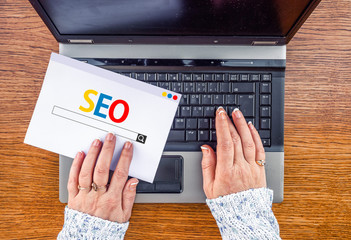  woman hands on laptop and seo optimization on paper sheet