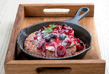 Breakfast in a pan on a white background. Pancakes with cream and jam. On a wooden tray.