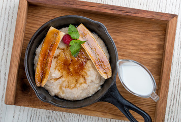 Breakfast in a pan on a white background. Oatmeal with banana and syrup. On a wooden tray.