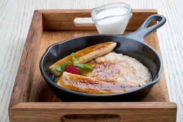 Breakfast in a pan on a white background. Oatmeal with banana and syrup. On a wooden tray.