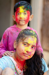 Cute adorable siblings playing with colours during holi festival of colors Indian asian caucasian creative portrait