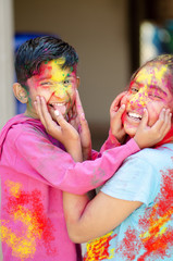 Cute adorable siblings playing with colours during holi festival of colors Indian asian caucasian creative portrait