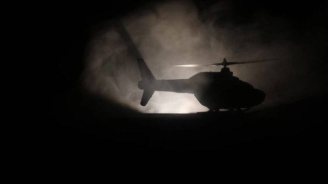 Silhouette of military helicopter ready to fly from conflict zone. Decorated night footage with helicopter starting in desert with foggy toned backlit. Selective focus. War concept