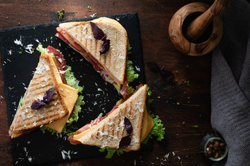 A club sandwich on a dark table with ham, cheese, bacon and lettuce.