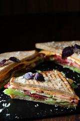 A club sandwich on a dark table with ham, cheese, bacon and lettuce close-up.