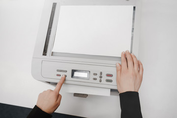 The hands of a young woman is placing a piece of paper on a flatbed scanner in preparation for copying it