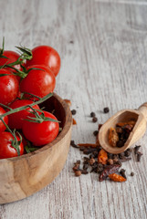 Vertical close-up of red cherry tomatoes in wooden bowl with spices