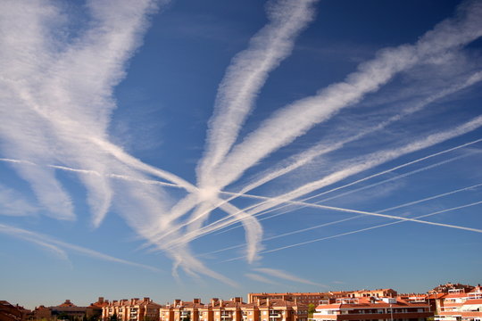 Many chemtrails or contrails  produced by airplanes flying on blue sky over the city.  conspiracy theory or biological agents