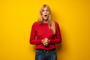 Blonde woman over yellow wall with surprise and shocked facial expression