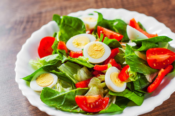spinach salad with eggs, pepper and tomatoes in white plate on wooden table background