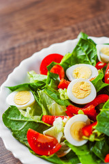 spinach salad with eggs, pepper and tomatoes in white plate on wooden table background
