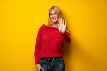 Blonde woman over yellow wall counting five with fingers