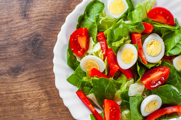 spinach salad with eggs, pepper and tomatoes in white plate on wooden table background