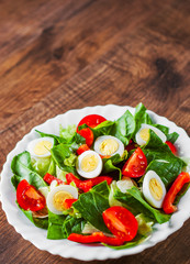 spinach salad with eggs, pepper and tomatoes in white plate on wooden table background