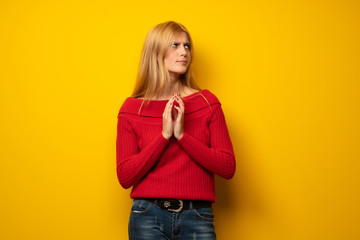 Blonde woman over yellow wall scheming something