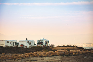 Motorhome making wild camp on the beach at a beautiful sunset or sunrise with mountains in the background. Caravan parked on the beach in front of the blue sea in a beautiful place of wild nature