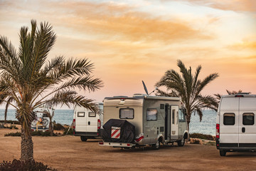 Motorhome making wild camp on the beach at a beautiful sunset or sunrise with mountains in the background. Caravan parked on the beach in front of the blue sea in a beautiful place of wild nature - obrazy, fototapety, plakaty