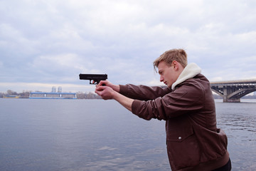 A young man in a jacket shoots with a gun near the river in the city.