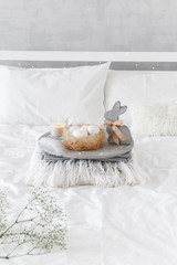 Fototapeta na wymiar White modern bedroom with Easter decoration. Bed with white bedding set, concrete tray, nest with white eggs, decorative bunny figure, candle and gypsophila flowers.