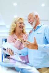 Obraz premium Delighted smiling Caucasian couple discussing about tablet and standing in tech store. Man holding tablet.