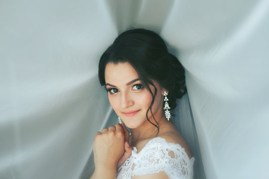 Portrait of beautiful bride in white dress on white veil background