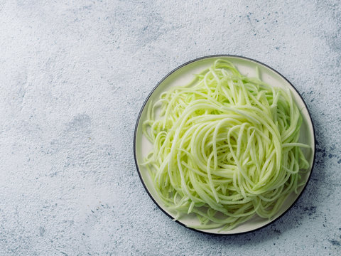 Zucchini Noodles On Plate. Vegetable Noodles - Green Zoodles Or Courgette Spaghetti On Plate Over Gray Background. Clean Eating, Raw Vegetarian Food Concept. Copy Space For Text. Top View Or Flat Lay