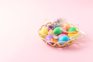 Fototapeta na wymiar Decorative Easter eggs with feathers in basket on pink background. Easter composition, greeting card with multicolored decorative eggs pastel rose background.
