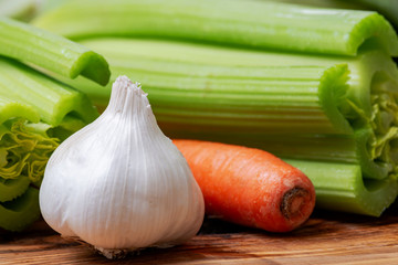 Fresh Raw Organic Celery Stalks, Garlic and Orange Carrots arranged on natural olive wood. 